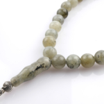 Toptan doğal taş labradorit tesbih, gri zemin üzerinde mavi ve yeşil yansımalarıyla sezgiyi güçlendiren, manevi kullanım ve koleksiyon için ideal doğal taş tesbih