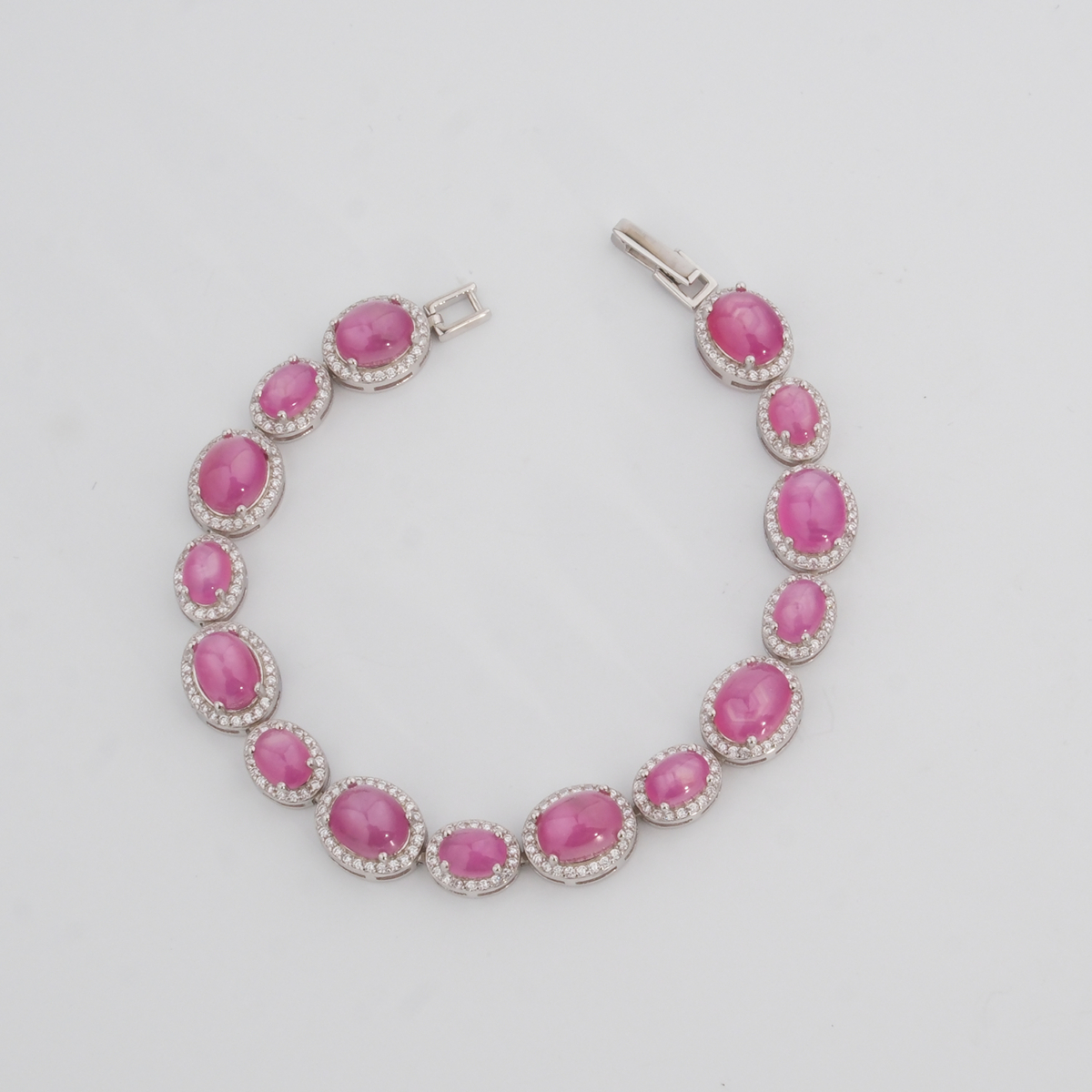 Pulsera elegante de plata de ley 925 para mujer con rubíes rojo-rosado tallados en cabujón y rodeados por marcos ovales de circonitas, exhibida en 1.jpg.