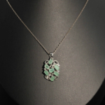 A luxury designer necklace featuring original faceted oval emerald gemstones arranged in a sterling silver filigree pendant with zircon accents.