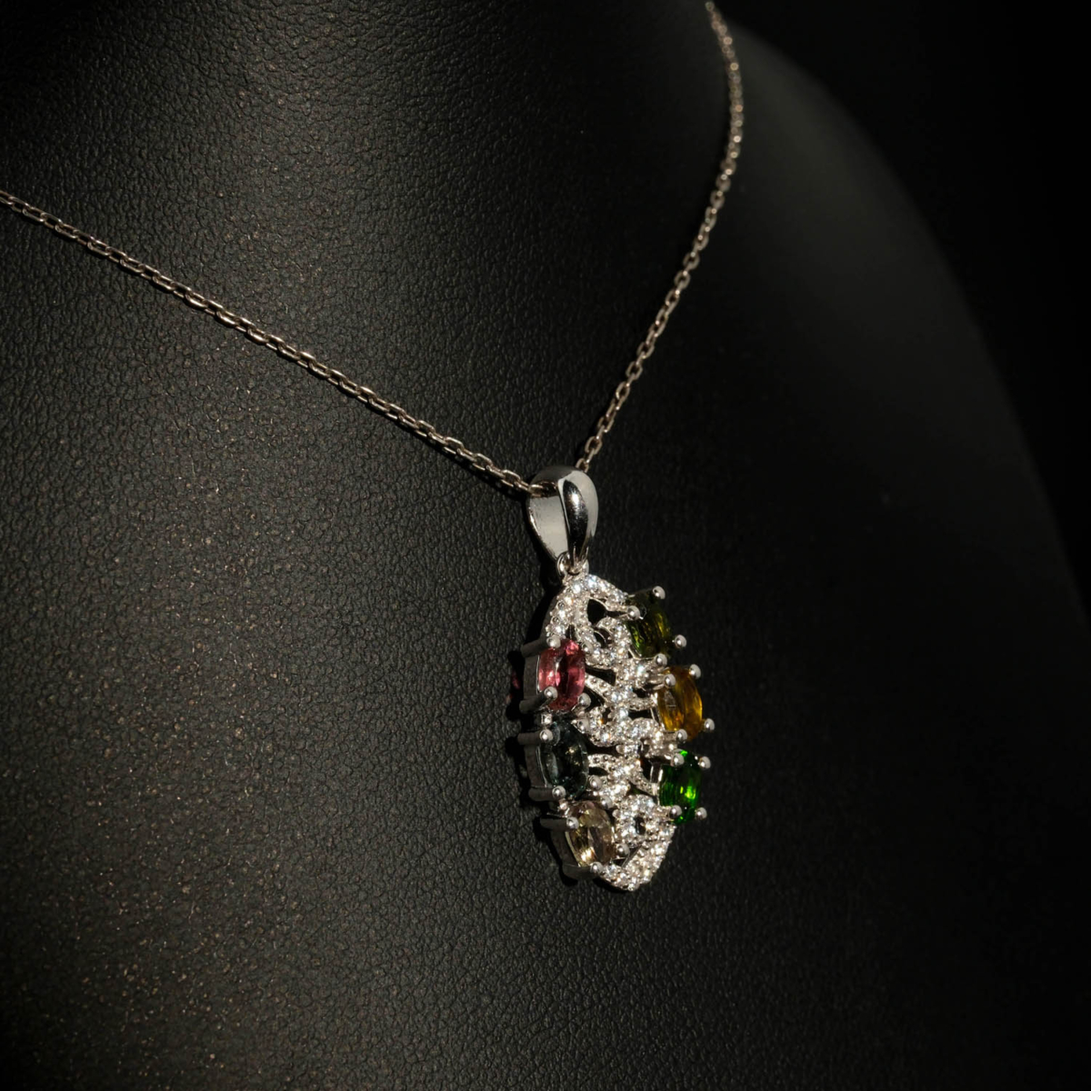 A luxury designer necklace featuring original faceted oval multicolor tourmaline gemstones arranged in a sterling silver filigree pendant with zircon accents.