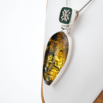 Collectible handcrafted 925 sterling silver necklace with a teardrop-shaped original natural amber stone, decorated with dark green enamel work and elegant silver motifs.