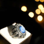 Bague pour homme en argent 925 ornée d'une pierre naturelle de saphir étoilé original de taille cabochon ovale et d'un entourage magistralement gravé.