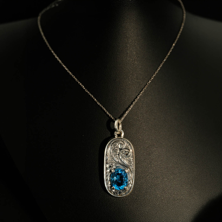 Halskette aus 925er Sterlingsilber mit einem oval facettierten, originalen Blautopas-Naturstein und meisterhaft gravierter Einfassung.