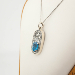 Halskette aus 925er Sterlingsilber mit einem oval facettierten, originalen Blautopas-Naturstein und meisterhaft gravierter Einfassung.