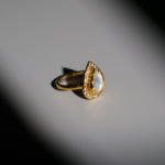 A luxury women's statement ring featuring a pear-cut original moonstone gemstone surrounded by cubic zirconia with enamel details in gold plated 925 sterling silver.