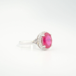 A delicate women's statement ring featuring an oval-cut original ruby gemstone surrounded by cubic zirconia halo in 925 sterling silver.