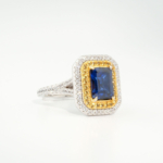 A luxury women's statement ring featuring a 1.85ct radiant-cut original blue sapphire gemstone surrounded by yellow and white cubic zirconia double halo in 925 sterling silver.