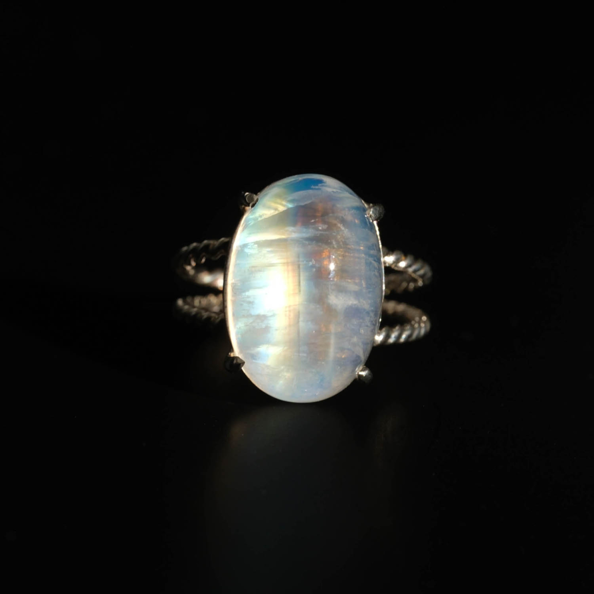 A luxury women's statement ring featuring a large original oval cabochon moonstone with intense blue sheen on a twisted 925 sterling silver band.