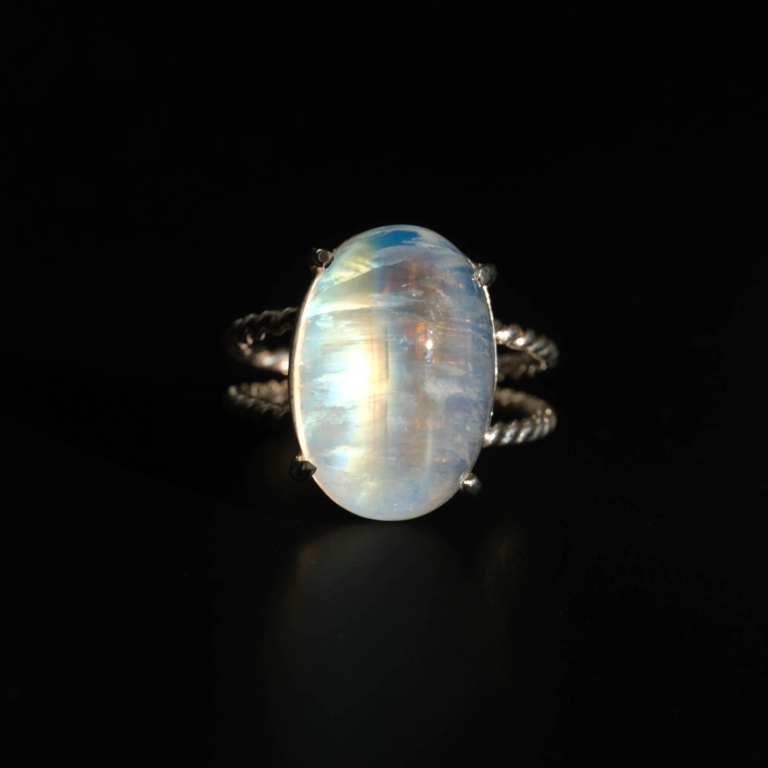 A luxury women's statement ring featuring a large original oval cabochon moonstone with intense blue sheen on a twisted 925 sterling silver band.