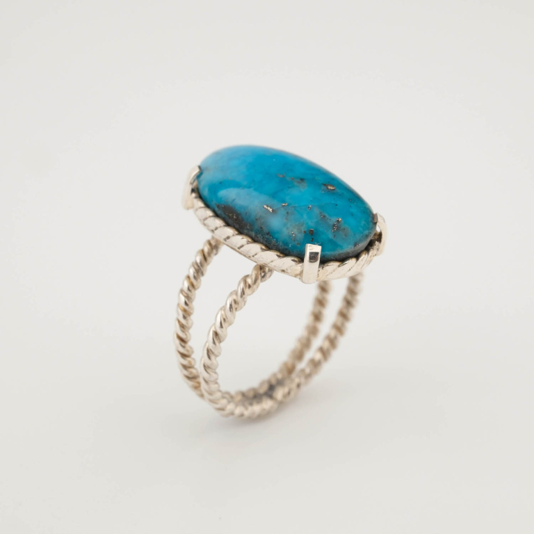 A luxury women's statement ring featuring a large original oval cabochon turquoise with natural matrix on a twisted 925 sterling silver band.