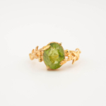 A luxury women's statement ring featuring an original oval faceted peridot gemstone set in a gold-plated 925 sterling silver artisan twig and leaf design.