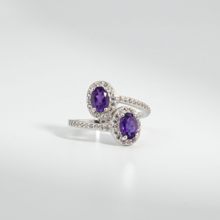 A 925 sterling silver women's bypass ring featuring two natural oval cut purple amethyst gemstones with cubic zirconia halo.