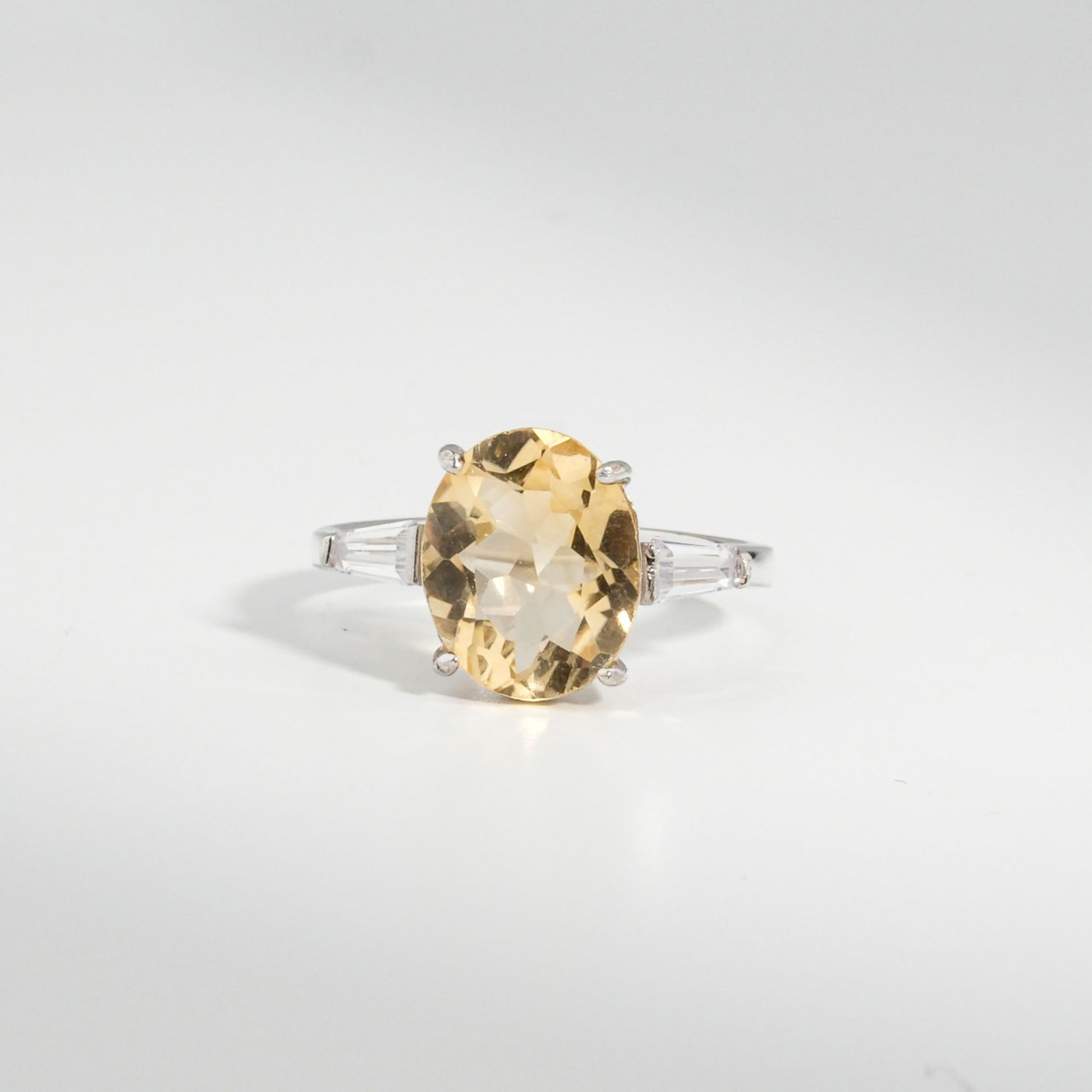 A 925 sterling silver women's ring featuring a natural oval faceted yellow citrine gemstone flanked by baguette cubic zirconia stones.
