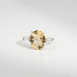 A 925 sterling silver women's ring featuring a natural oval faceted yellow citrine gemstone flanked by baguette cubic zirconia stones.