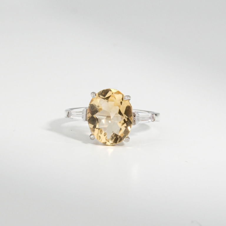 A 925 sterling silver women's ring featuring a natural oval faceted yellow citrine gemstone flanked by baguette cubic zirconia stones.