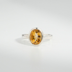 A 925 sterling silver women's ring featuring a natural oval faceted yellow citrine gemstone in a smooth bezel setting.