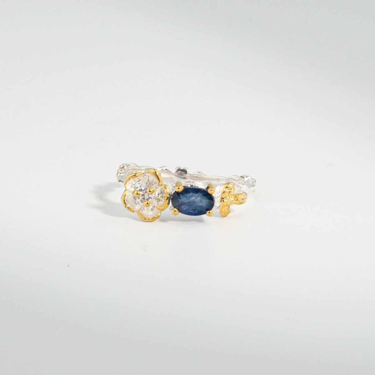 A 925 sterling silver women's ring featuring a natural oval blue sapphire gemstone accented with a gold-plated silver flower motif.