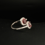 A 925 sterling silver women's bypass ring featuring two natural oval cut red garnet gemstones with cubic zirconia halo.