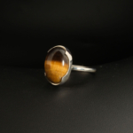 A 925 sterling silver women's ring featuring a natural oval cabochon tiger's eye gemstone with chatoyant golden brown bands.