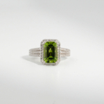 A 925 sterling silver women's ring featuring a 3.33 ct natural baguette cut green peridot gemstone surrounded by cubic zirconia halo.