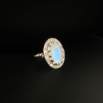 A 925 sterling silver women's ring featuring a 3.5 ct natural oval cabochon blue sheen moonstone gemstone surrounded by cubic zirconia halo.