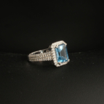 A 925 sterling silver women's ring featuring a natural baguette cut neon blue topaz gemstone surrounded by cubic zirconia halo.
