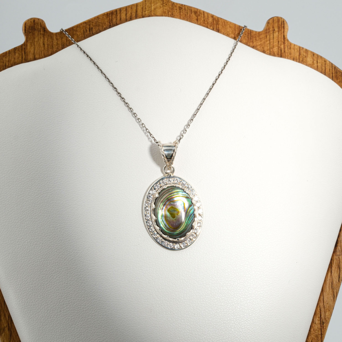 A 925 sterling silver unisex pendant featuring a natural oval cabochon iridescent abalone shell gemstone surrounded by cubic zirconia halo.