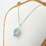 Faceted oval natural blue topaz gemstone pendant necklace in 925 sterling silver shining on black fabric.