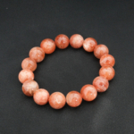 A natural shimmering peach-orange sunstone gemstone stretch bracelet with smooth 13-14mm round beads.