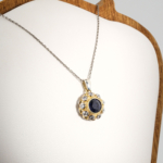 Pendentif pour femme en argent 925 serti d'un saphir bleu naturel entouré de zircons et de détails dorés.