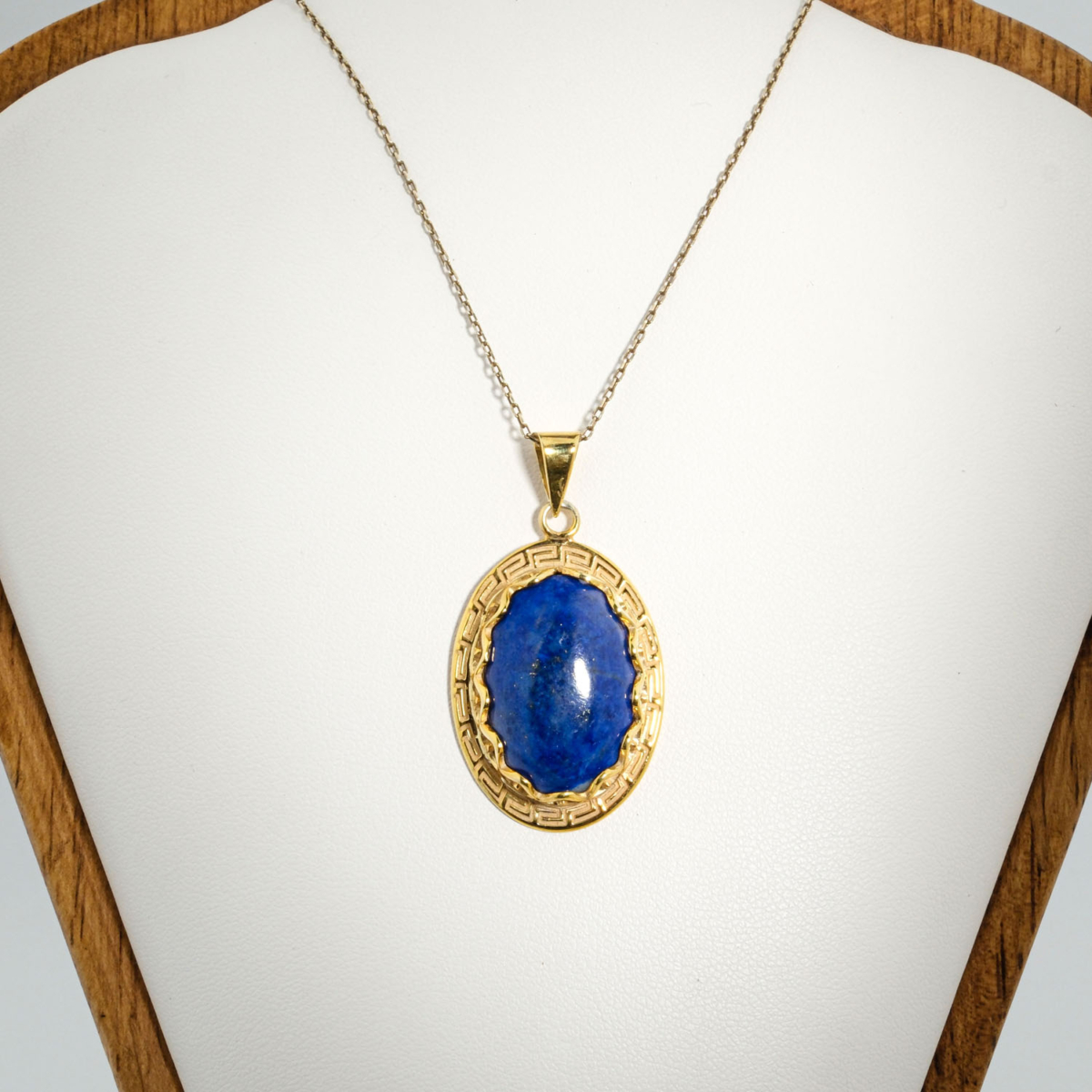 A gold-plated 925 sterling silver unisex pendant featuring a natural oval cabochon lapis lazuli gemstone surrounded by a Greek key pattern bezel.