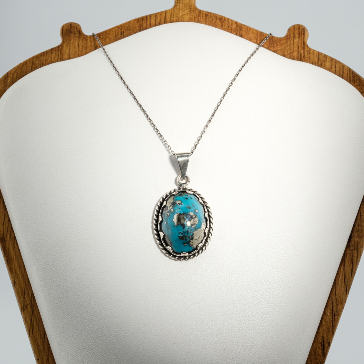 A 925 sterling silver handmade unisex pendant featuring a natural high oval cabochon cut Nishapur turquoise gemstone with pyrite spots.