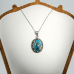 A 925 sterling silver handmade unisex pendant featuring a natural high oval cabochon cut Nishapur turquoise gemstone with pyrite spots.