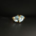 A gold-plated 925 sterling silver women's ring featuring two natural pear-shaped faceted blue topaz gemstones in a prong setting.