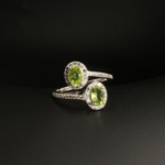 A 925 sterling silver women's bypass ring featuring two natural oval cut green peridot gemstones with cubic zirconia halo.