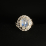 A 925 sterling silver women's ring featuring a natural oval cabochon blue sheen moonstone gemstone surrounded by cubic zirconia halo.