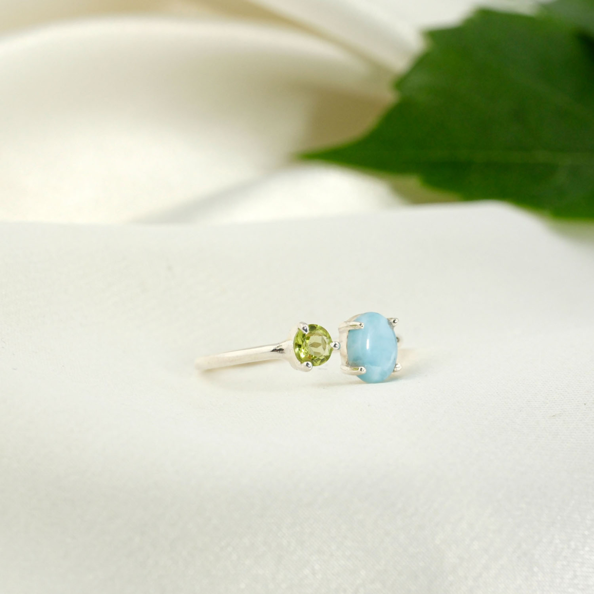 A 925 sterling silver women's bypass ring featuring a natural oval cabochon sea-blue larimar and a round faceted green peridot gemstone.