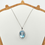 Pendentif halo pour femme avec topaze bleue naturelle ovale et argent 925 étincelant sur fond noir.